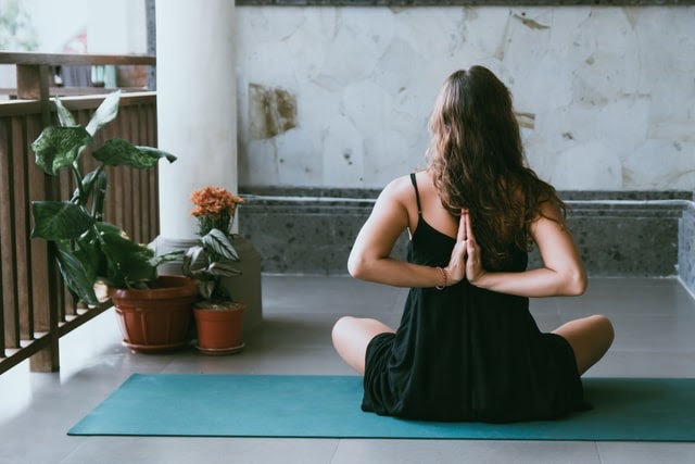 Woman in a black dress sitting on a blue yoga mat and meditating